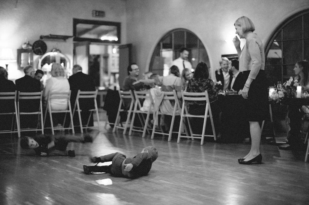 A child lying on the dance floor while adults dine and converse in the background.