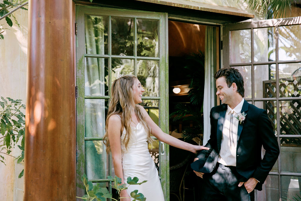 Bride and groom sharing a playful moment outside a rustic building.