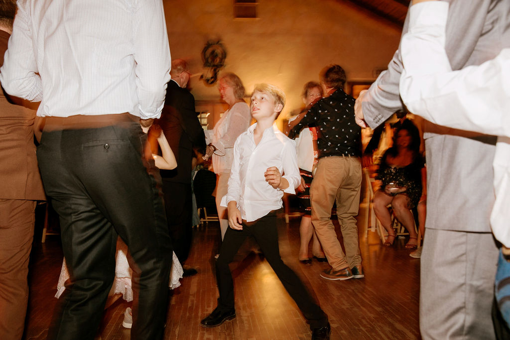 A young boy dancing confidently on a dance floor surrounded by adults.