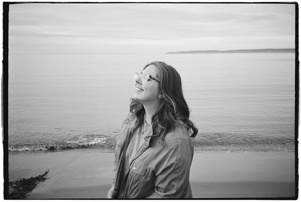 Woman smiling with closed eyes, standing by the seaside.
