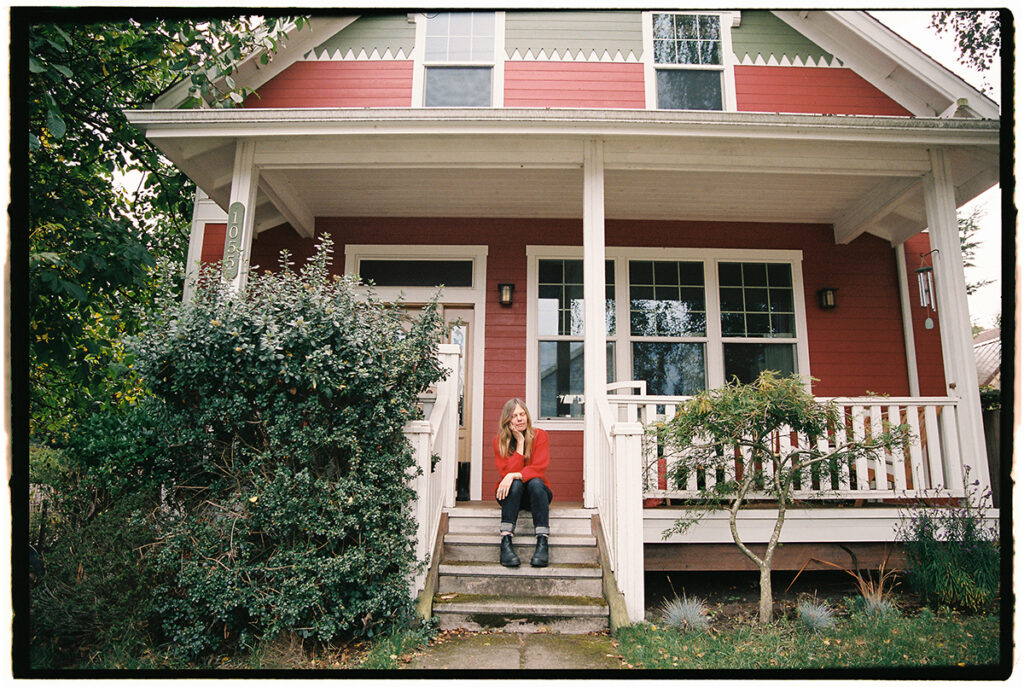 Woman sitting on the steps of a red house with a porch.