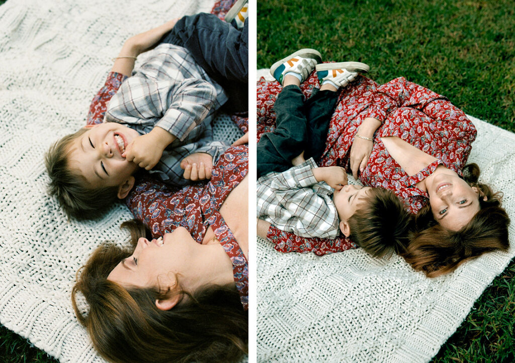 A mother enjoys a playful and affectionate moment with her young son while lying on a blanket on the grass.