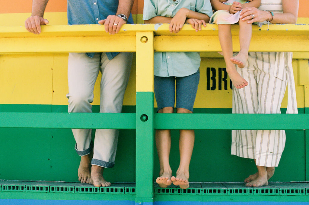 Four people of varying heights standing behind a yellow and green railing, with only their lower halves visible.