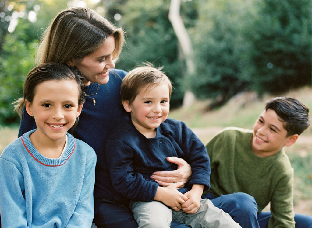 A family of four with three children smiling outdoors.