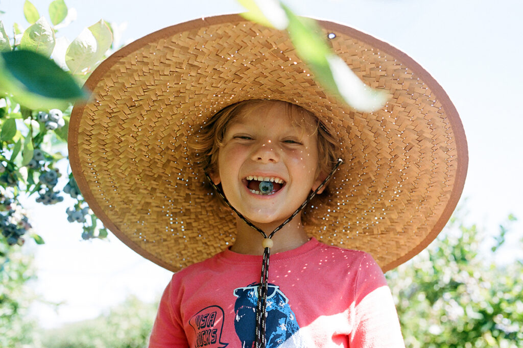A joyful child wearing a large straw hat smiling outdoors.